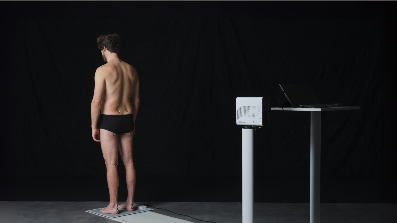 Junger Mann in Unterwäsche steht vor einem Tisch mit Laptop, vor schwarzem Hintergrund.